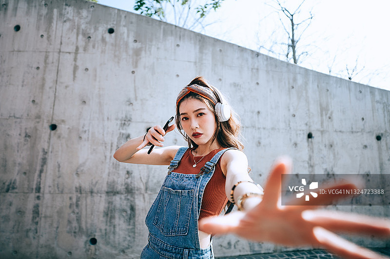 在户外混凝土墙边戴耳机听音乐跳舞的亚洲年轻女子 портрет图片素材