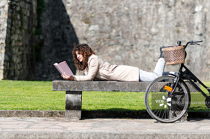 躺在混凝土长椅上看书的卷发女人图片素材