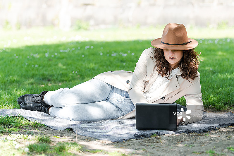 躺在草地上毯子上使用笔记本电脑的卷发美女图片素材