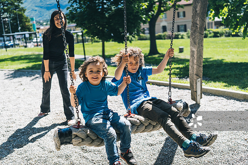 母亲在操场上推着秋千上的小男孩图片素材