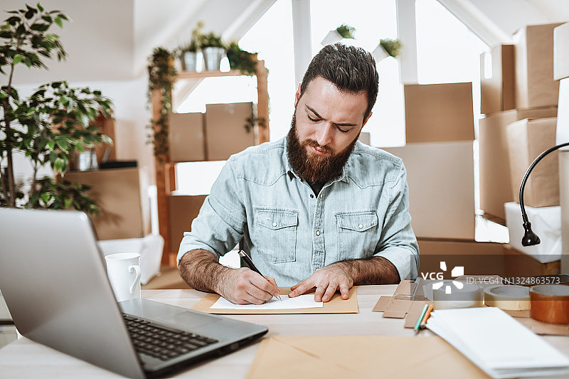 在配送中心给顾客写信的络腮胡男职工图片素材