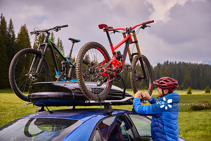 男子从车顶行李架上取下山地自行车图片素材
