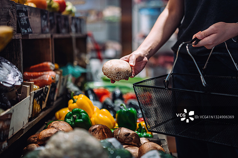 年轻女子在当地杂货店购买新鲜有机农产品（局部），挑选蘑菇。绿色生活，健康饮食，支持本地商业理念图片素材