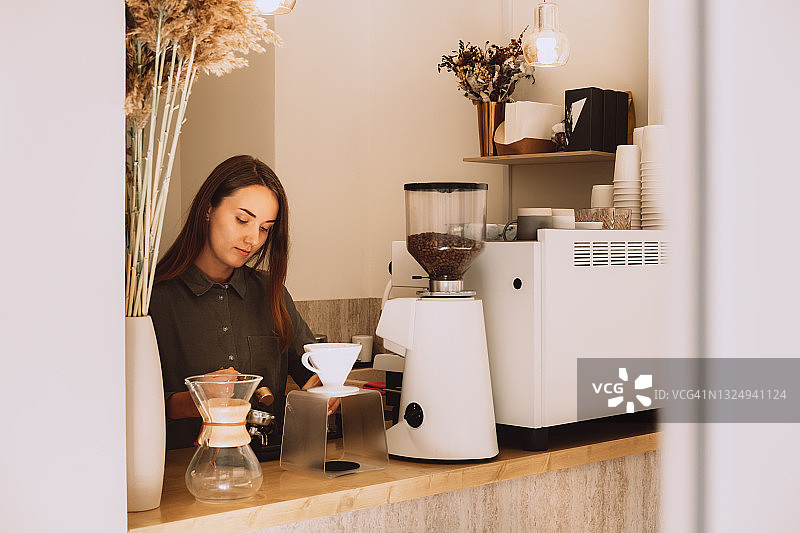 年轻女咖啡师在咖啡店吧台后制作咖啡图片素材
