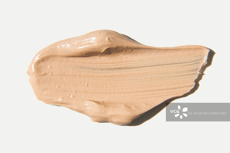 涂抹遮瑕膏，在白色背景上涂抹粉底。浅棕色或米色液体粉末。BB霜，CC霜，奶油彩妆质地。图片素材