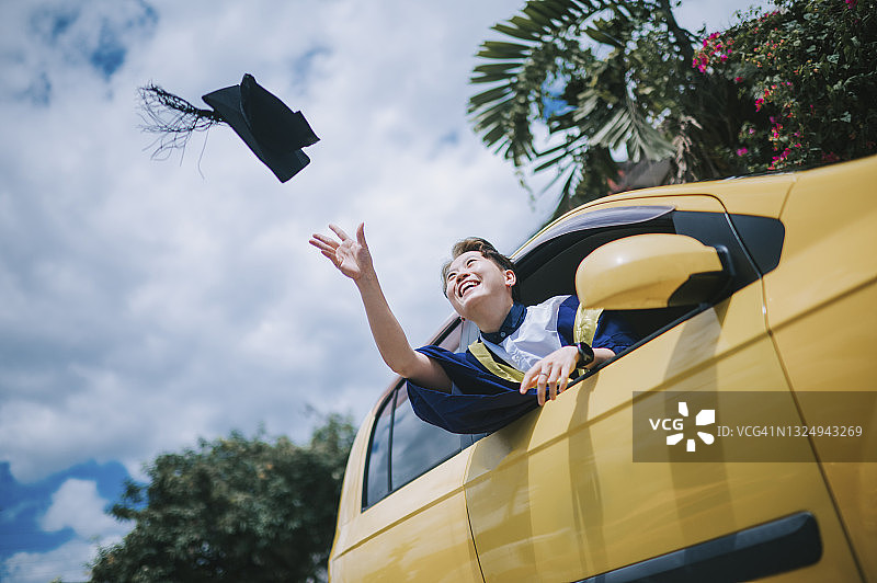 中国年轻女子穿着毕业礼服，在车里笑着扔学士帽图片素材