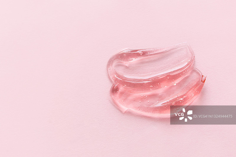 粉红色背景上粉红色凝胶的透明涂抹。液体透明质酸凝胶。平放，俯视图，复制空间图片素材