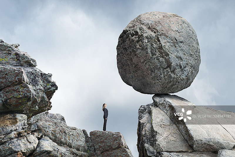 女人抬头看着悬在她上方摇摇欲坠的巨石图片素材