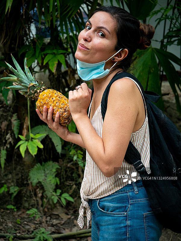 拉丁裔女人口罩拉到下巴处，右手拿菠萝看向镜头图片素材