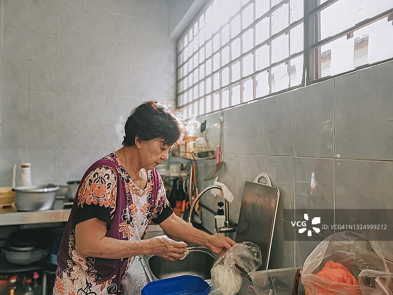 亚洲华人妇女在厨房做饭，在水槽里洗菜图片素材