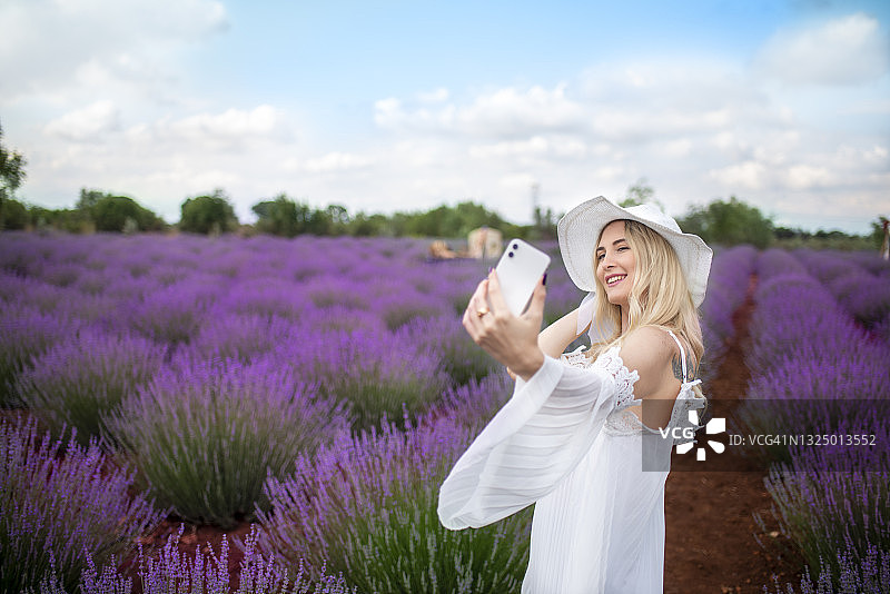 金发年轻美丽女人在薰衣草田里拍自拍图片素材