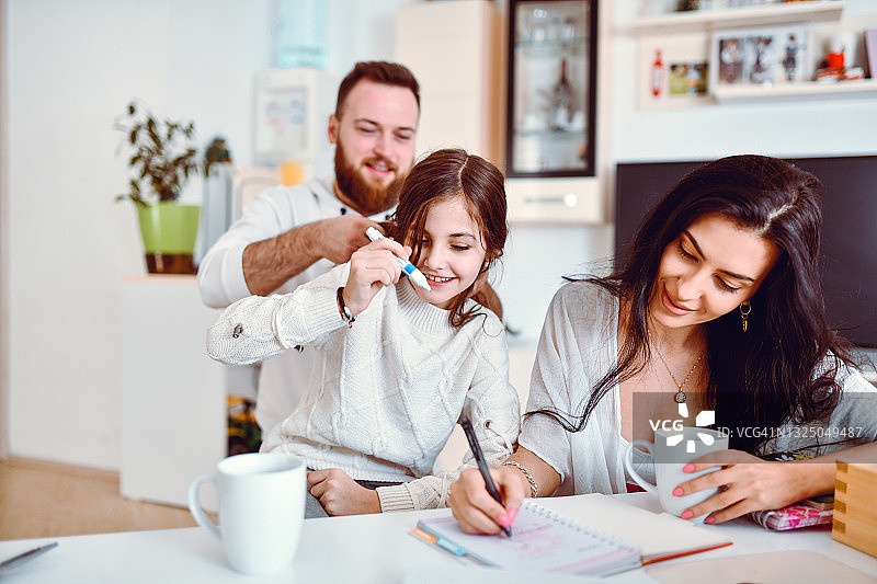 男人在妻子和女儿一起做功课时为她们编发图片素材