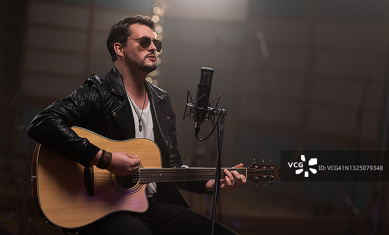 男子弹奏原声吉他照片，男子坐在录音室麦克风前图片素材