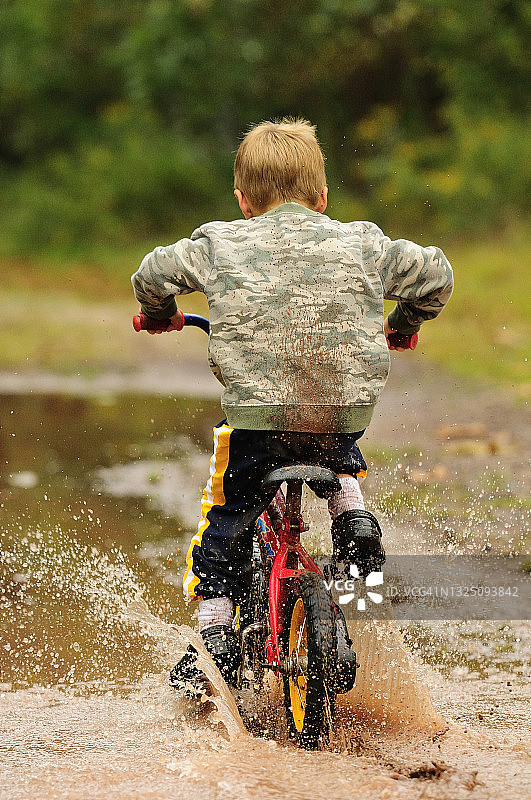 小男孩骑自行车穿过泥地图片素材