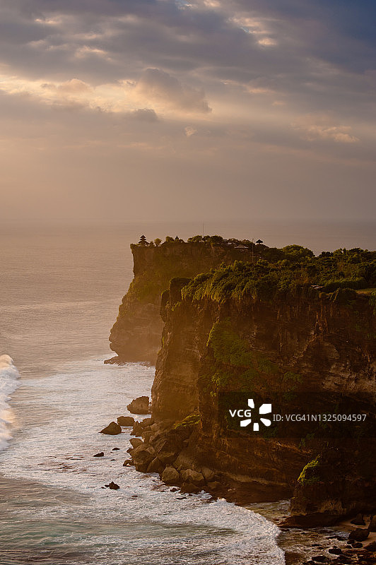 日落时分，海浪拍打着高耸的树木覆盖的悬崖图片素材
