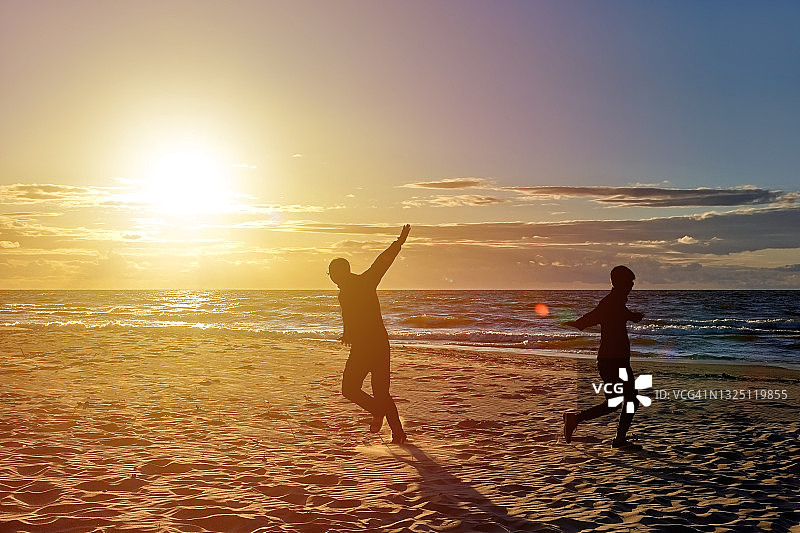 在海滩上奔跑的男人和男孩剪影图片素材