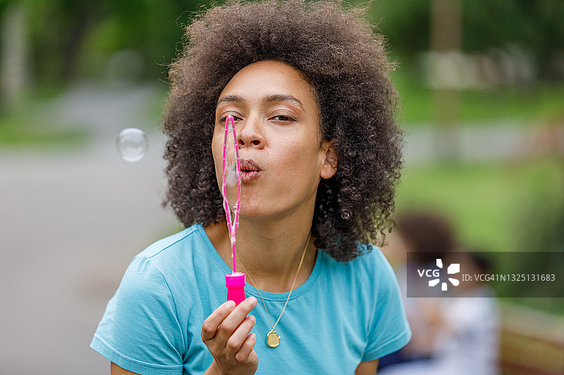 年轻的母亲在绿草如茵的公园里散步并吹泡泡图片素材