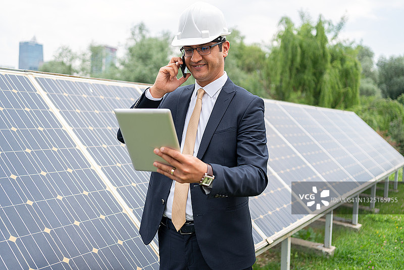 戴安全帽的男经理工程师在太阳能电站用平板电脑检查太阳能电池板系统运行图片素材