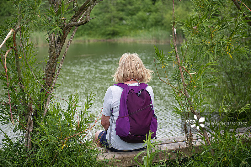 一位中年女徒步旅行者在长椅上休息，俯瞰着湖面图片素材