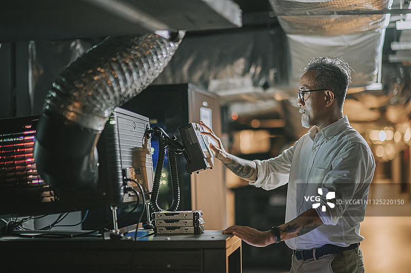 在现代电影放映室后台操作电脑的亚裔老年男性图片素材