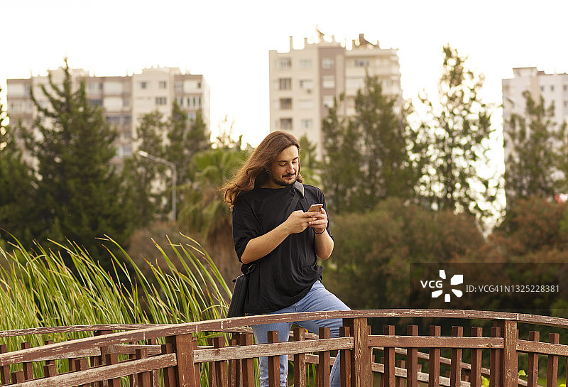 在公园里发短信的长发英俊男人图片素材