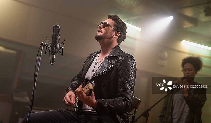 多种族音乐家在录音室录制唱片，弹奏电吉他和唱歌图片素材