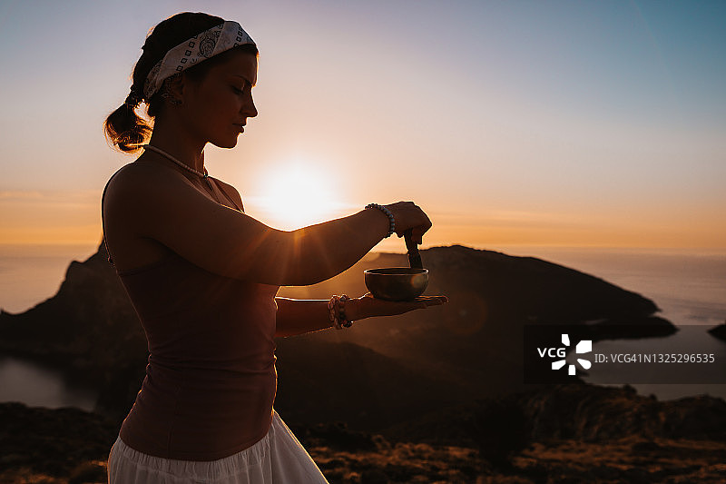 日出山海景观中的年轻女性藏族颂钵剪影图片素材
