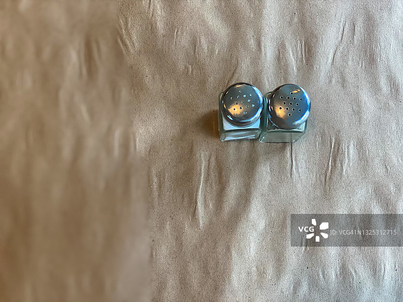 棕色纸覆盖的桌子上玻璃盐和胡椒瓶的俯视图图片素材