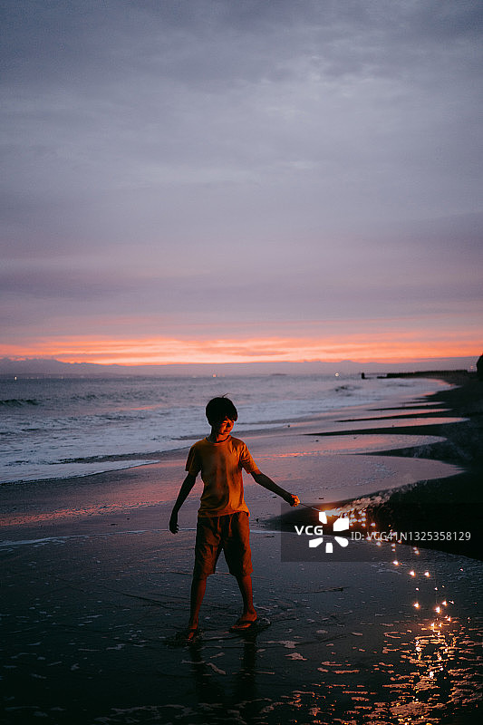 小男孩在黄昏的海滩上玩烟花棒图片素材
