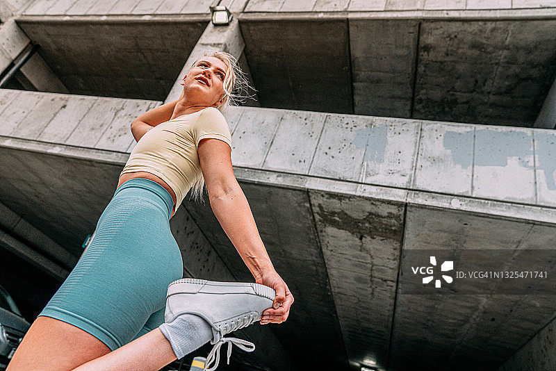 年轻白人女性户外跑步：四头肌拉伸低角度英雄镜头图片素材