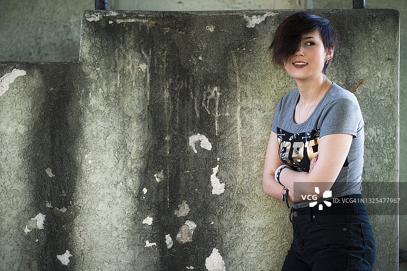 在破旧墙前，用头发遮住一只眼睛的少女图片素材