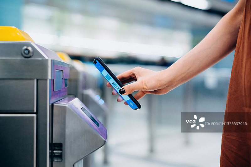 年轻的亚洲女性扫描二维码，在地铁站办理登机手续，通过智能手机为地铁票进行快速简便的非接触式支付的手部特写。NFC技术，即触即走概念图片素材