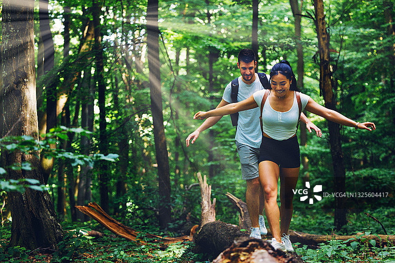 情侣在森林徒步旅行时跨越断树图片素材