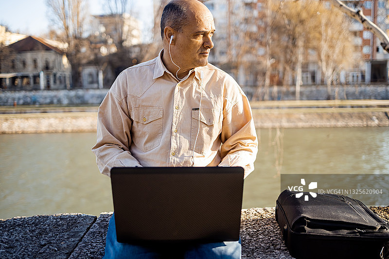 坐在城市码头使用笔记本电脑的中年商人图片素材