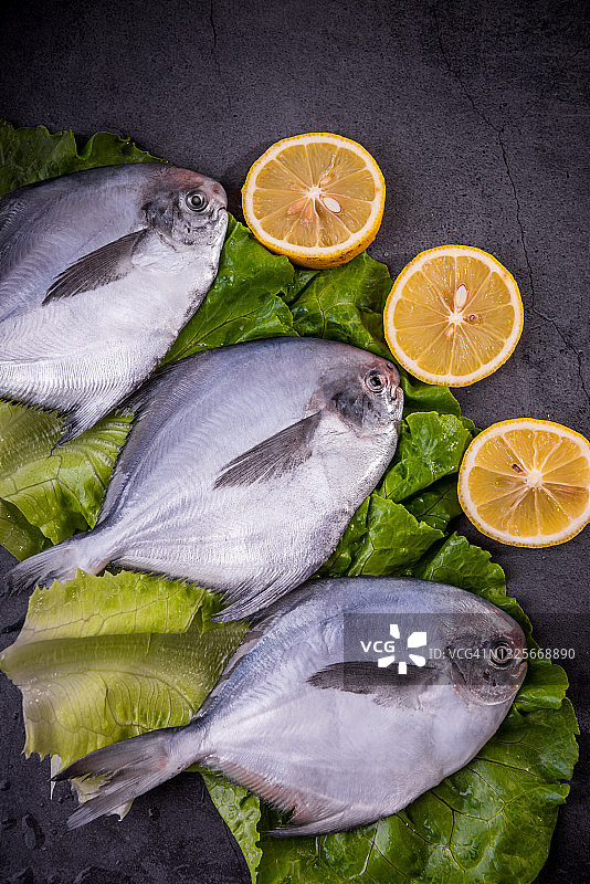 木板上放着香草、香料和柠檬的新鲜鲳鱼图片素材