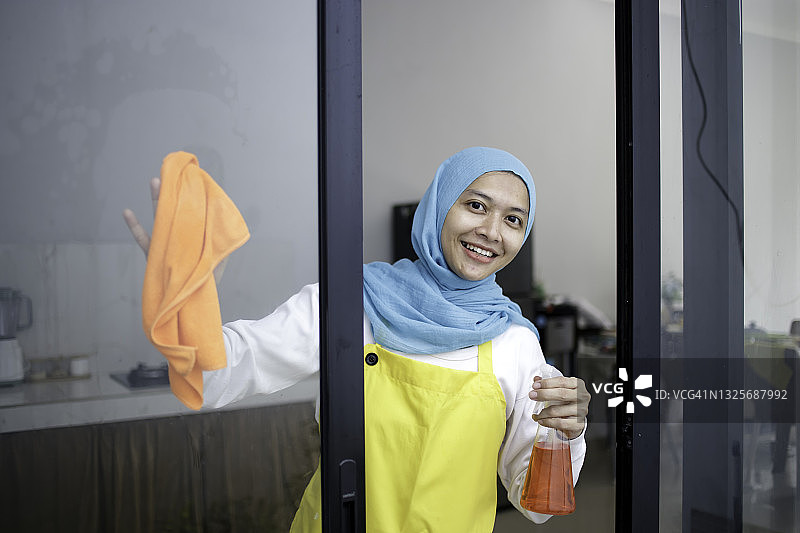 戴着头巾的亚洲年轻女子清洁玻璃推拉门图片素材