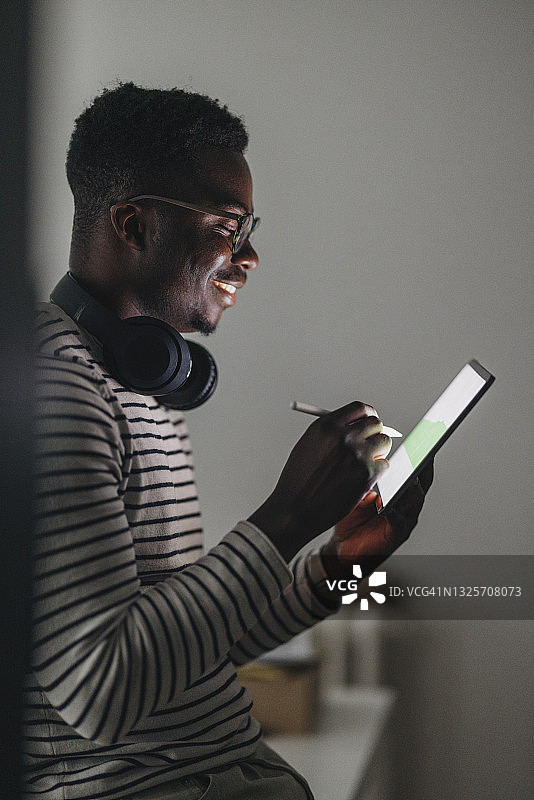 在家工作：使用平板电脑和笔的年轻快乐的非洲裔美国人图片素材