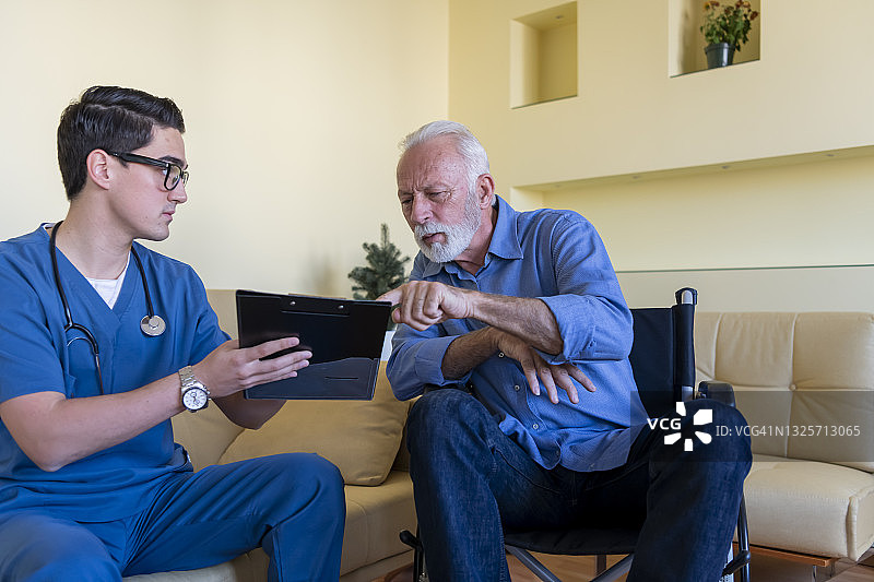 穿蓝色制服的年轻男医生拜访坐轮椅的老年男子图片素材