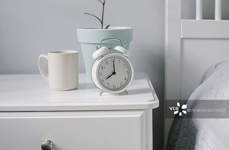 卧室床头柜上的白色闹钟、米色咖啡杯、茶和室内植物，营造早晨的概念图片素材