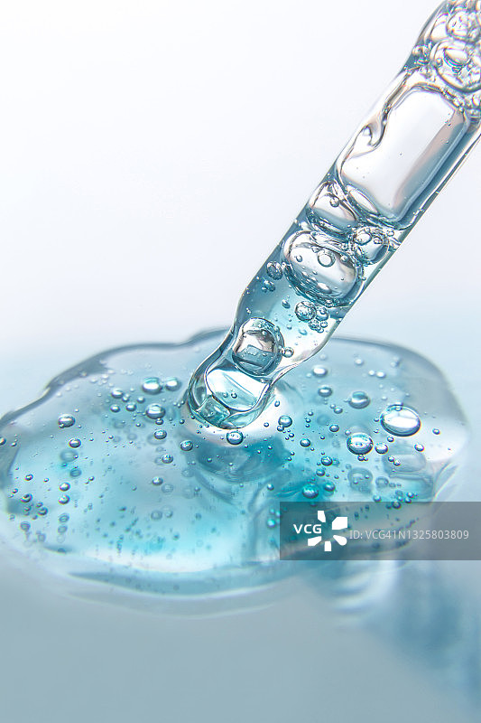 蓝色背景下用滴管吸取的液体凝胶或精华液滴特写，含肽、神经酰胺、透明质酸凝胶的美容产品，扁平风格，顶部视角，复制空间图片素材