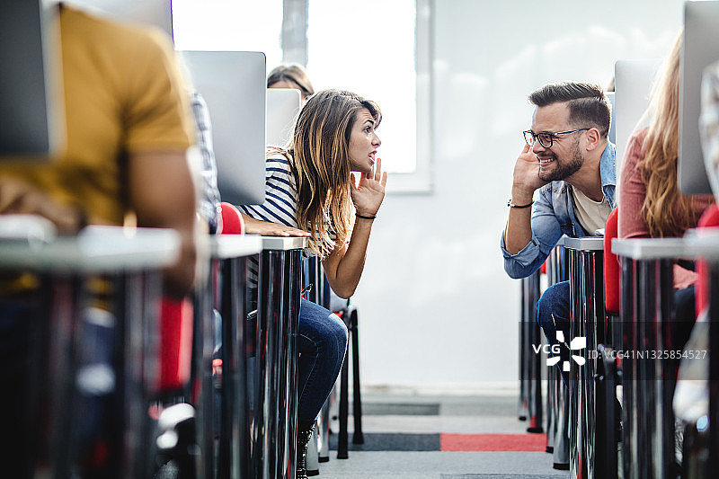 年轻的学生在计算机课上窃窃私语。图片素材