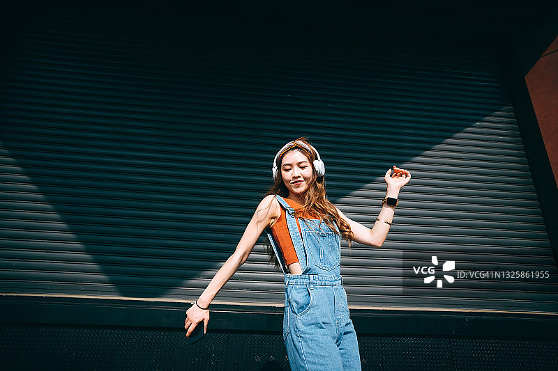 年轻亚洲女性户外彩色墙前戴耳机听音乐舞蹈图片素材