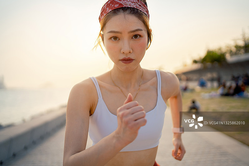 坚定的亚洲年轻女运动员在户外锻炼的肖像，在城市海滨长廊的城市公园跑步，日落时分。积极的生活方式。健康和健身概念图片素材