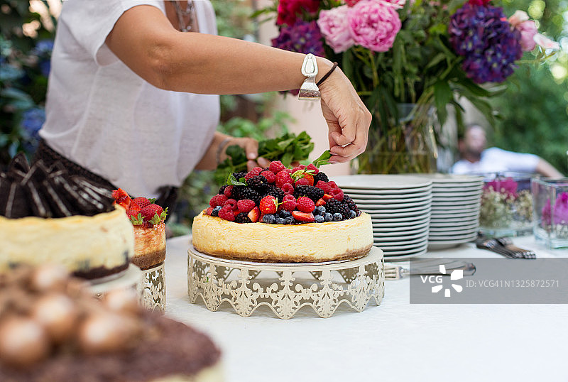 女人在浆果芝士蛋糕中加入新鲜的薄荷叶图片素材