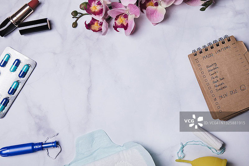 俯视角度拍摄的记事本，内有经期用品、止痛药和兰花图片素材