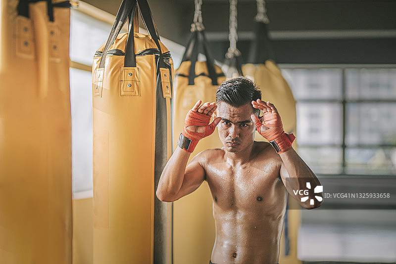 马来西亚泰拳男运动员在健身房拳击袋旁图片素材