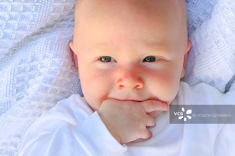 穿白色衬衫的快乐宝宝在白色毯子上吮吸手指图片素材