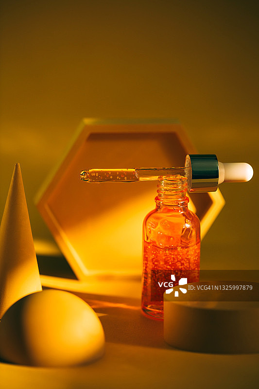 透明橙色玻璃滴管瓶，面部精华和颗粒置于黄色背景抽象领奖台附近。2021年流行色，正面视角图片素材