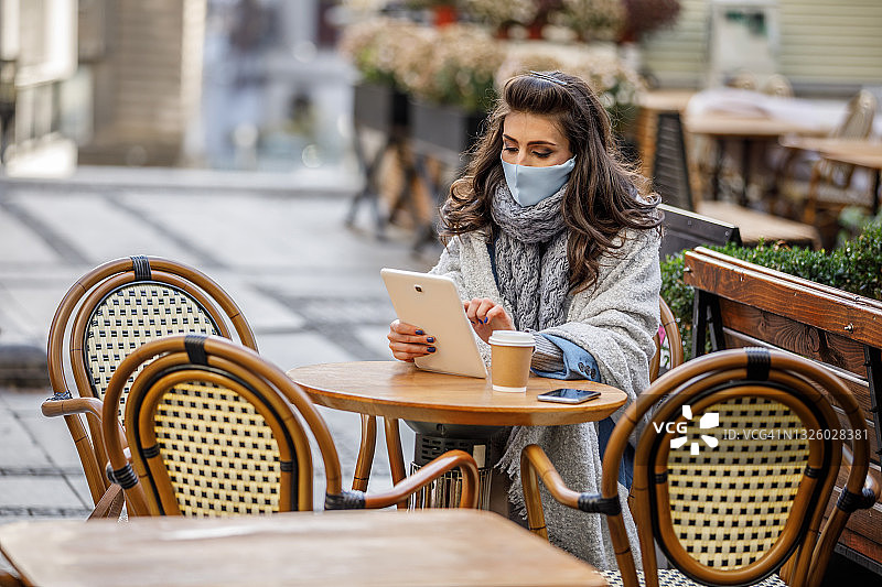 戴着面膜坐在餐厅里喝咖啡和上网的美丽女人图片素材