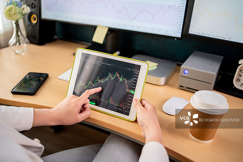 卧室里穿白色西装的亚洲股市投资者正在用电脑和平板查看股票图表图片素材